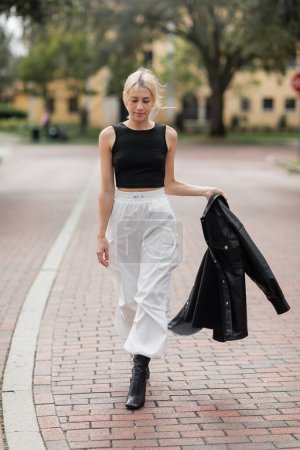 Junge Frau in weißen Cargohosen und Stiefeln läuft mit schwarzer Hemdjacke auf der Straße in Miami  