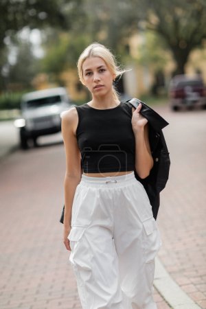 young woman in white cargo pants and tank top walking with black shirt jacket on street in Miami 