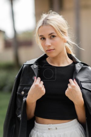 Téléchargez les photos : Portrait de jeune femme blonde en cuir noir veste chemise regardant caméra - en image libre de droit