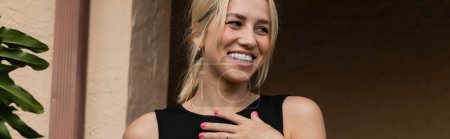 Photo for Cheerful young woman in black tank top standing near house in Miami, banner - Royalty Free Image