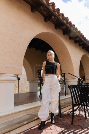 Blonde Frau in stylischem Outfit steht in der Nähe eines modernen Hauses in Florida 