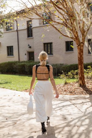 Rückansicht einer blonden Frau mit Handtasche, die in der Nähe ihres Hauses in Miami spaziert 