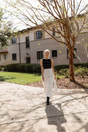 Blonde Frau mit Handtasche steht in der Nähe von Haus in Miami 