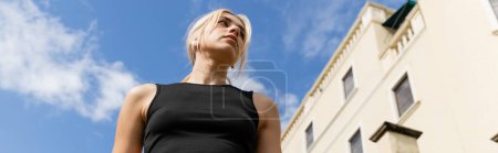low angle view of blonde woman in tank top standing near building in Miami, banner 