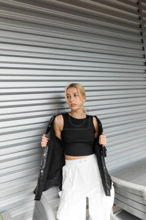 Junge blonde Frau im schicken Outfit steht in Miami vor Garagentor 