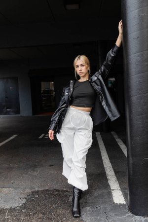 full length of young blonde woman in leather shirt jacket and cargo pants standing on street in Miami 