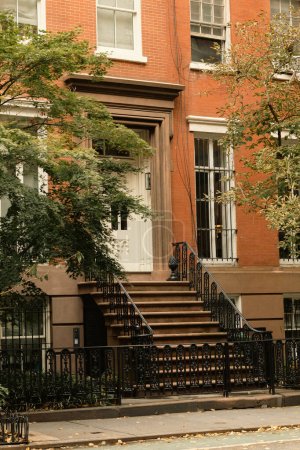 Backsteinhaus mit weißen Fenstern und Eingang mit Treppe in der Nähe von Herbstbäumen auf der Straße in New York City
