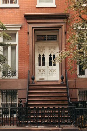 brick building with white door and stairs with metal railings and fence in New York City