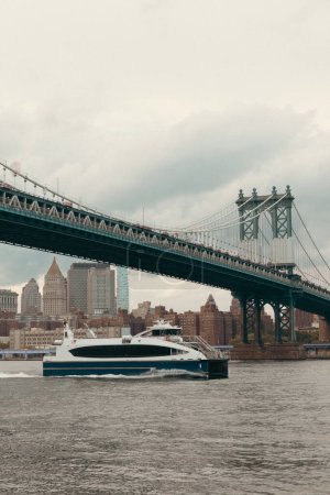 Moderne Jacht auf dem Hudson River unter Manhattan-Brücke und bewölktem Himmel in New York City