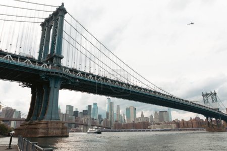 scenic view of Manhattan bridge and modern skyscrapers under cloudy sky in New York City