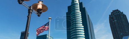vista de ángulo bajo de la linterna y la bandera de EE.UU. cerca de rascacielos bajo el cielo azul en la ciudad de Nueva York, bandera