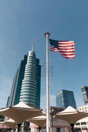 Foto de Usa flag and shade umbrellas near skyscrapers in Manhattan district of New York City - Imagen libre de derechos