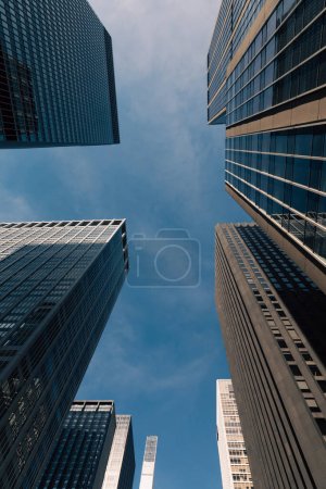 bottom view of contemporary high-rise buildings in Manhattan against blue and cloudy sky in New York City