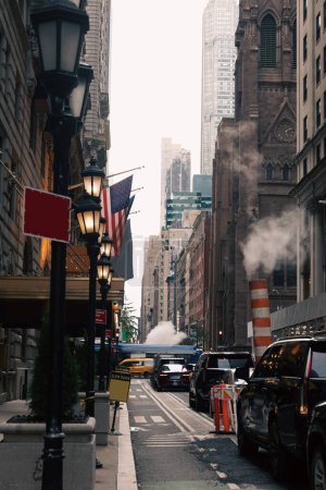 Foto de NEW YORK, USA - OCTOBER 13, 2022: narrow street with cars and lanterns near usa flags in Manhattan - Imagen libre de derechos