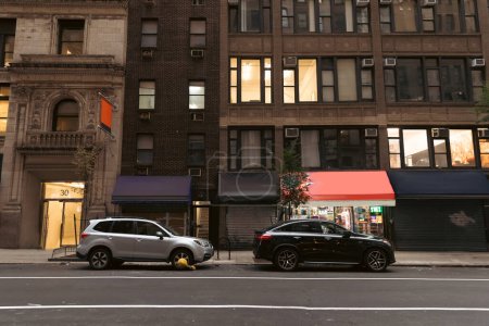 Foto de NEW YORK, USA - OCTOBER 13, 2022: cars near buildings with shops on road of urban street - Imagen libre de derechos