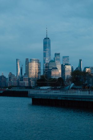 scenic cityscape with Manhattan skyscrapers and pier on Hudson river in dusk
