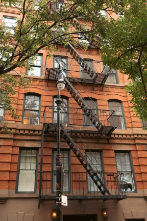Backstein-Wohnhaus mit Metallbalkonen und Brandfluchttreppe in der Nähe von Laternen und Bäumen in New York City