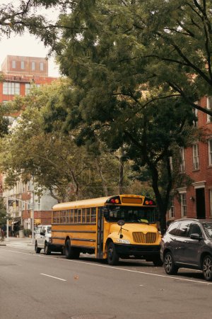 Foto de NUEVA YORK, EE.UU. - 13 de octubre de 2022: autobús escolar amarillo bajo los árboles de la calle urbana en el distrito de Brooklyn Height - Imagen libre de derechos
