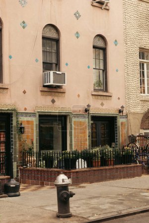 old building with arc windows near metal fence and flowerpots with plants in New York City