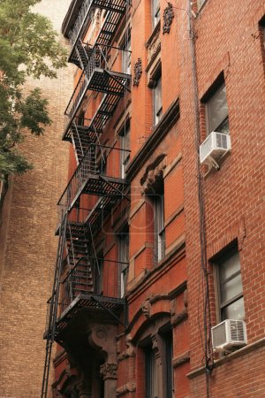 low angle view of brick building with metal balconies and fire escape ladders in New York City