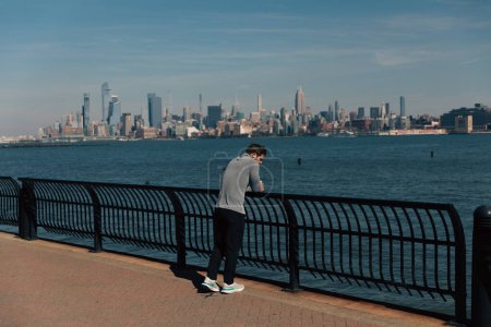 Foto de NUEVA YORK, EE.UU. - 11 de octubre de 2022: Hombre parado cerca de la valla de la pasarela costera del río Hudson - Imagen libre de derechos