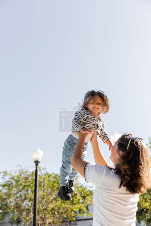 brunette mother in sunglasses lifting happy toddler daughter on street in Miami 