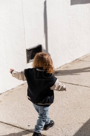 Foto de Vista trasera de la niña en chaqueta de bombardero elegante caminando por la calle en Miami - Imagen libre de derechos