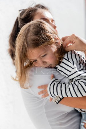 Téléchargez les photos : Mère attentionnée réconfortante bébé fille en chemise à manches longues rayée - en image libre de droit