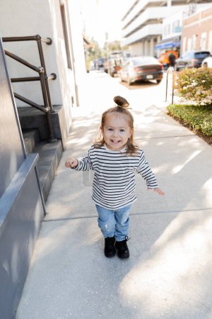 happy toddler girl in long sleeve shirt and blue jeans walking on street in Miami 