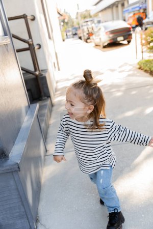 cheerful toddler child in long sleeve shirt and blue jeans walking on street in Miami 
