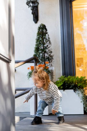 smiling baby girl in long sleeve shirt and blue jeans standing near house in Miami 