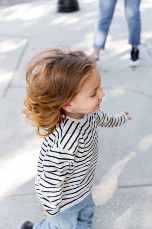 happy toddler girl in long sleeve shirt running near mother on blurred background 