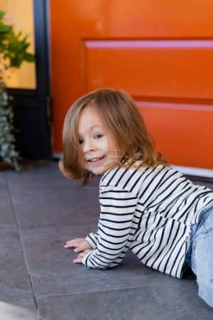 Foto de Feliz niño niña arrastrándose en el porche en el patio trasero contra la casa - Imagen libre de derechos