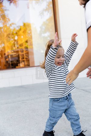 heureuse jeune fille debout avec les mains tendues près de la mère dans la rue à Miami 