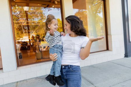 mère heureuse tenant dans les bras bébé fille près vitrine de magasin à Miami 
