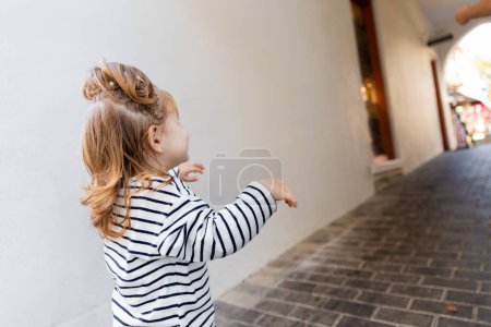 Téléchargez les photos : Tout-petit bébé fille à rayures chemise à manches longues regardant loin tout en marchant à l'extérieur - en image libre de droit