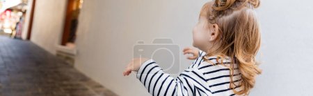 Téléchargez les photos : Bébé fille tout-petit en chemise à manches longues rayée regardant loin tout en marchant à l'extérieur, bannière - en image libre de droit