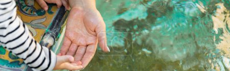 cropped view of mother and daughter holding hands near water in fountain, banner 