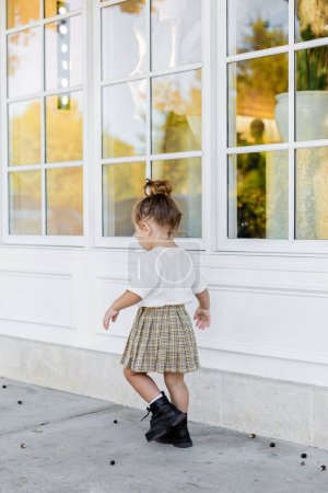 full length of toddler girl in skirt and white t-shirt walking near house 