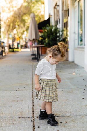full length of toddler girl in skirt and white t-shirt looking at ground on street in Miami 