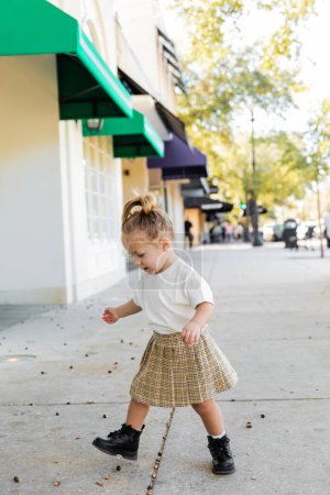 full length of toddler child in skirt and white t-shirt looking at acorns on ground in Miami 