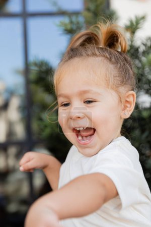 Porträt eines staunenden Kleinkindes im weißen T-Shirt, das lacht und wegschaut 