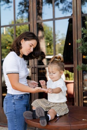 Nettes Kleinkind hält Händchen mit brünetter Mutter in der Nähe eines Cafés in Miami 