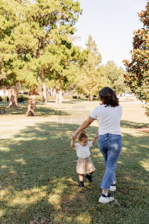 mère brune tenant la main avec fille heureuse tout-petit tout en jouant dans le parc de Miami 