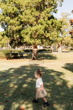 joyful baby girl in white t-shirt and skirt playing in green park 