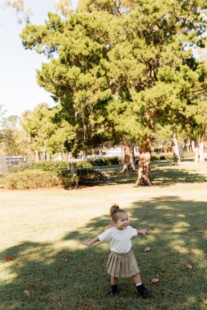 joyful baby girl standing with outstretched hands while playing in green park 