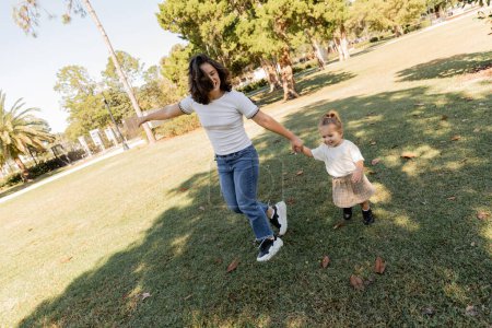 alegre madre e hijo tomados de la mano mientras juegan juntos en el verde parque de Miami 