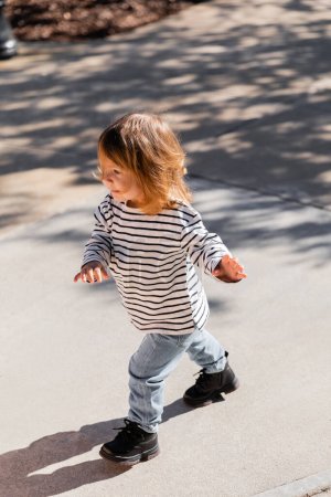 Hochwinkelaufnahme eines Kleinkindes in gestreiftem Langarmshirt und blauen Jeans, das auf der Straße in Miami läuft 