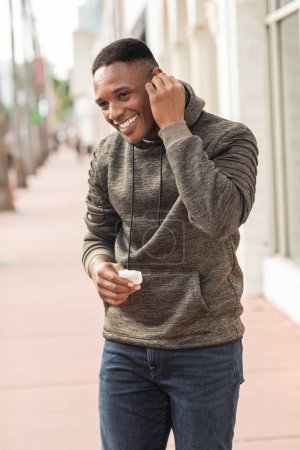 Lächelnder afrikanisch-amerikanischer Mann in Kapuzenpulli mit Kopfhörertasche auf der Straße in Miami 