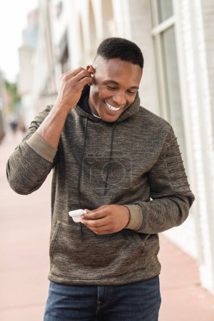 cheerful african american man in hoodie wearing wireless earphone on street in Miami 